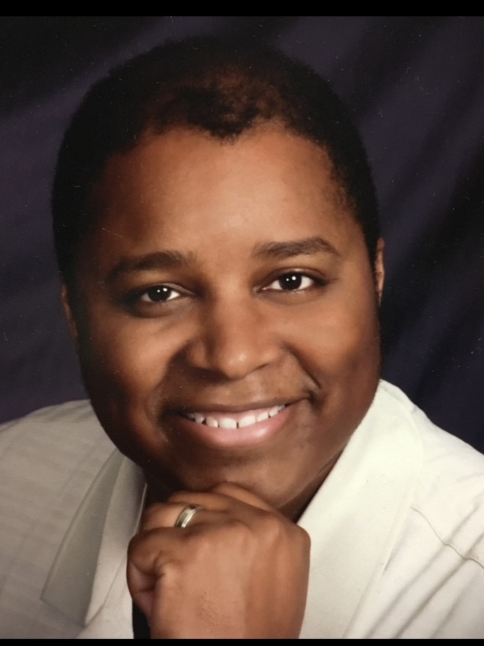 Head shot of Reverend Phillip E. Ross, Pastor of Bethel AME Church Portland OR he is in a thinker pose with a sweet honest smile showing teeth and wearing a white robe