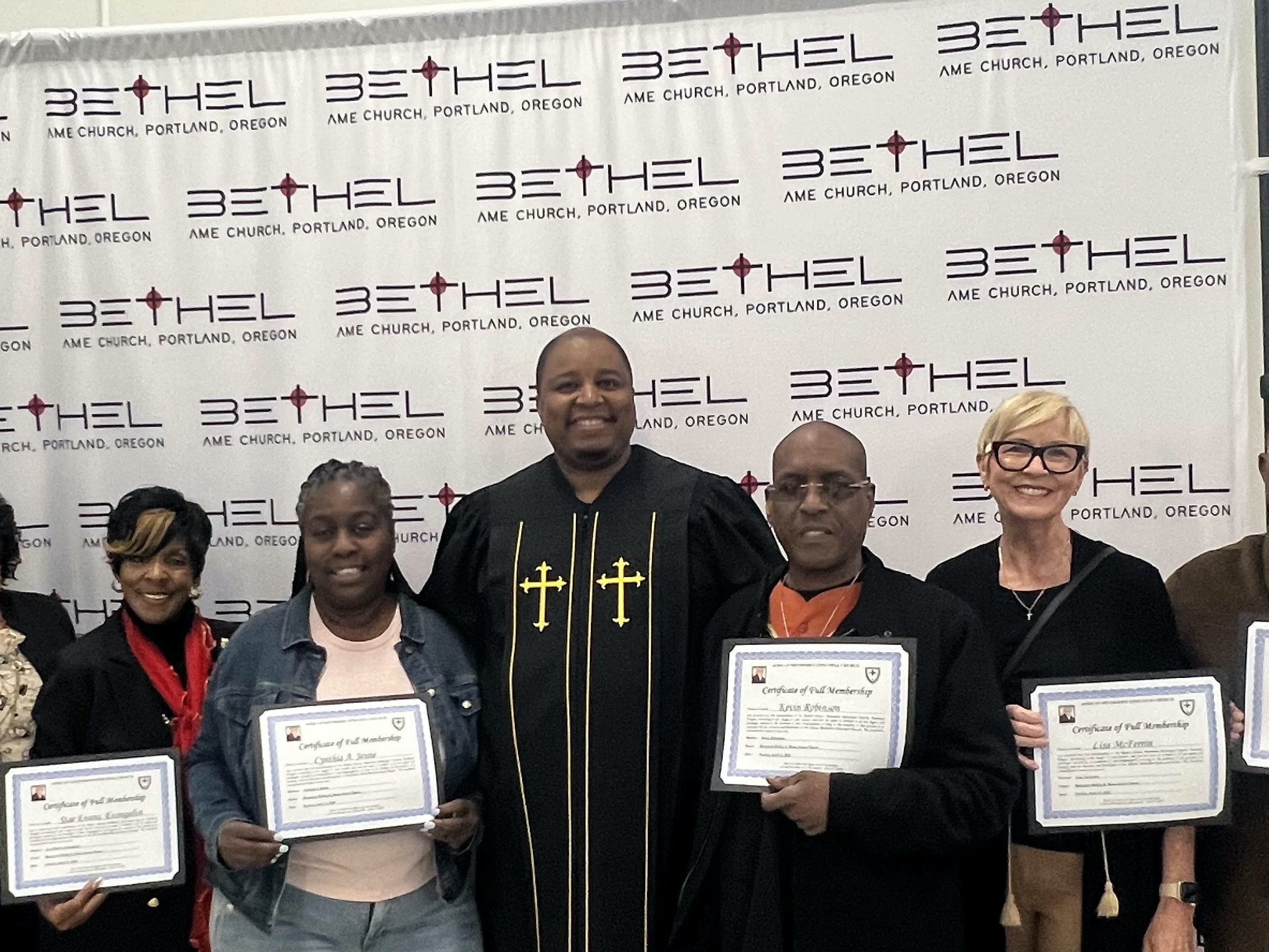 A group on new members holding certificates with Pastor Ross in the center of the group they have smiles on their face backdrop with Bethel AME Portland logo behind them.