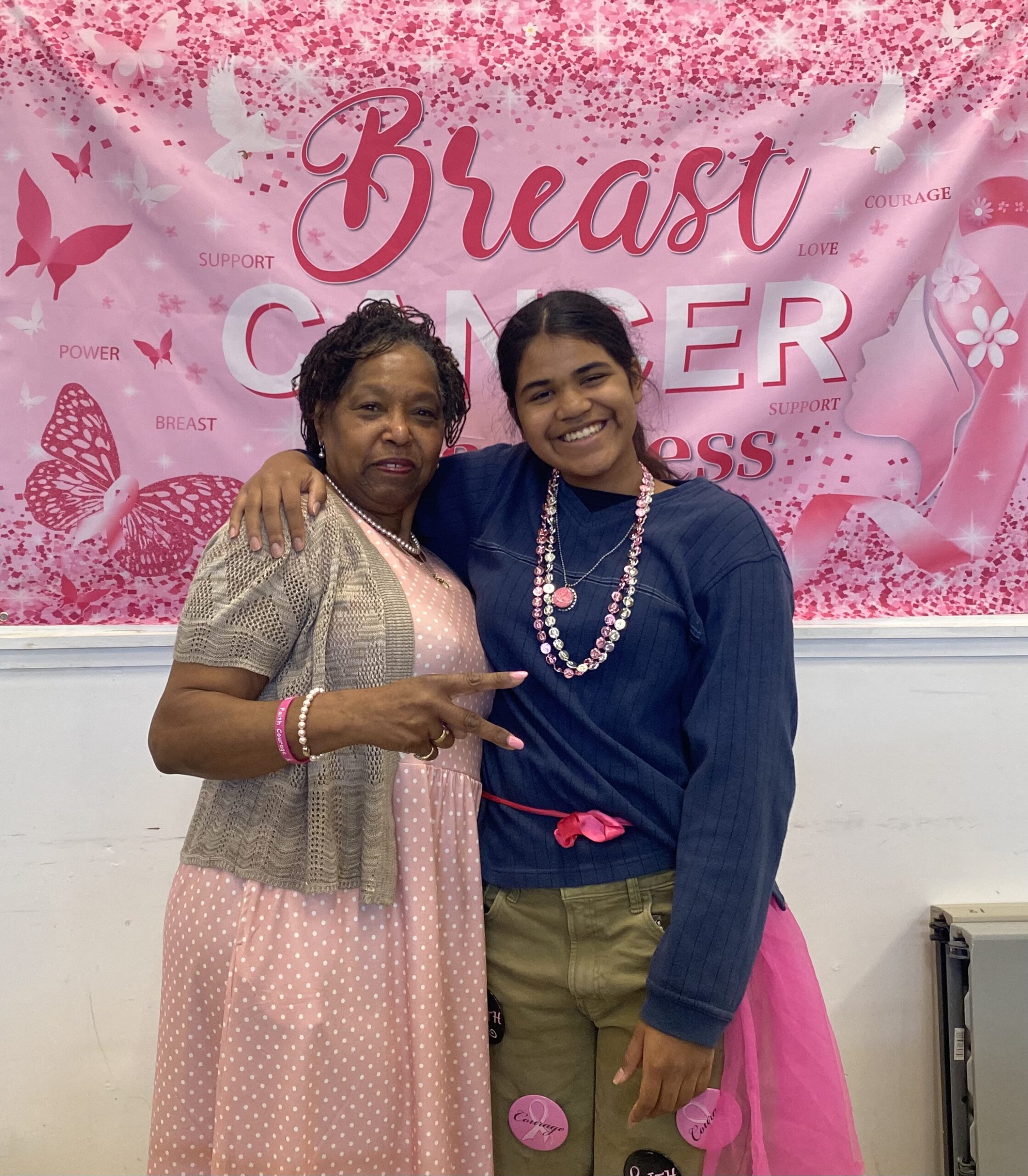 Carol Drayton & Harmony posing in the fellowship hall under the banner Breast Cancer - preporation for worship in pink